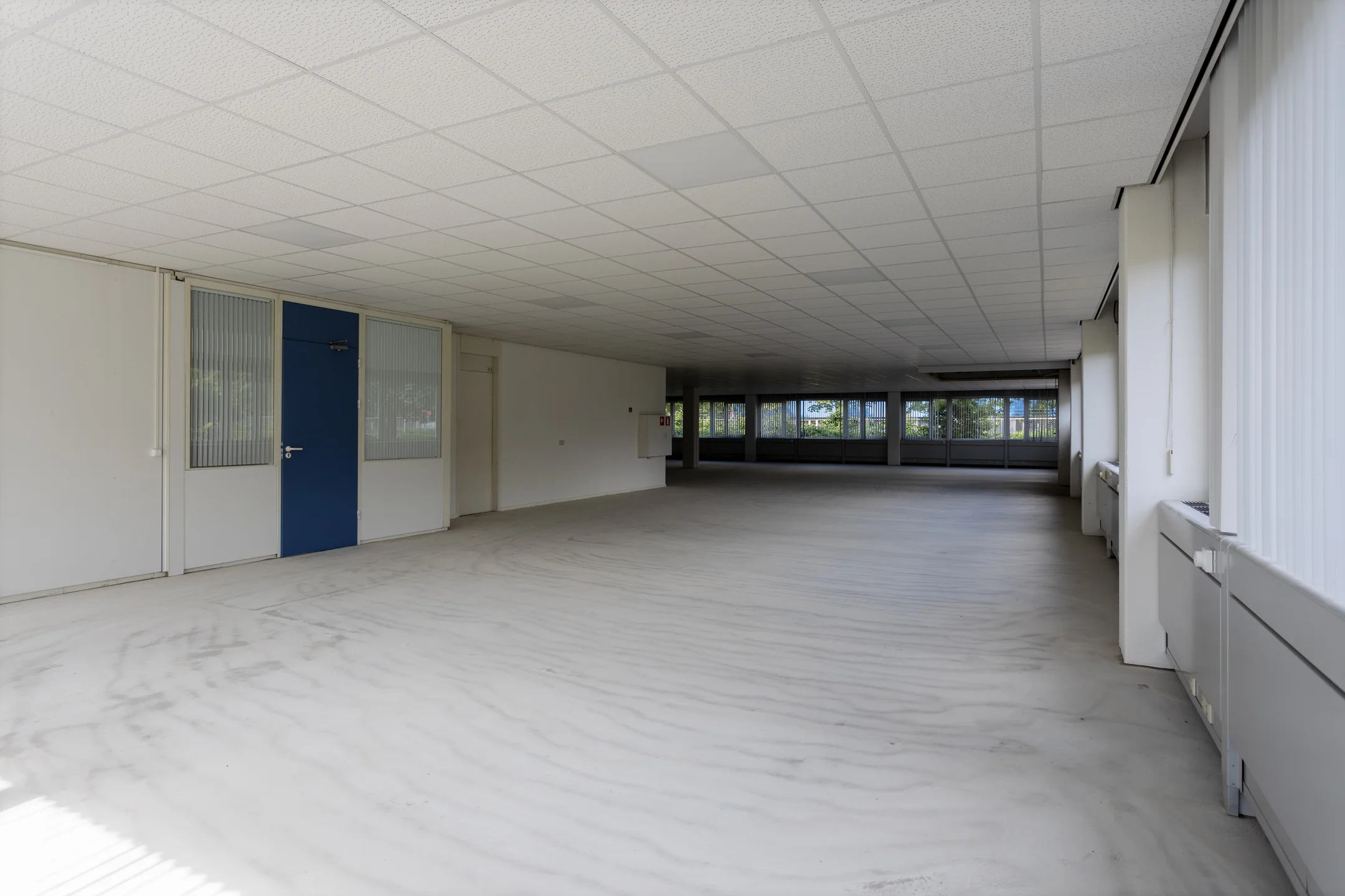 Lege kantoorruimte met systeemplafond, grote raampartijen en een blauwe deur aan de Energieweg.