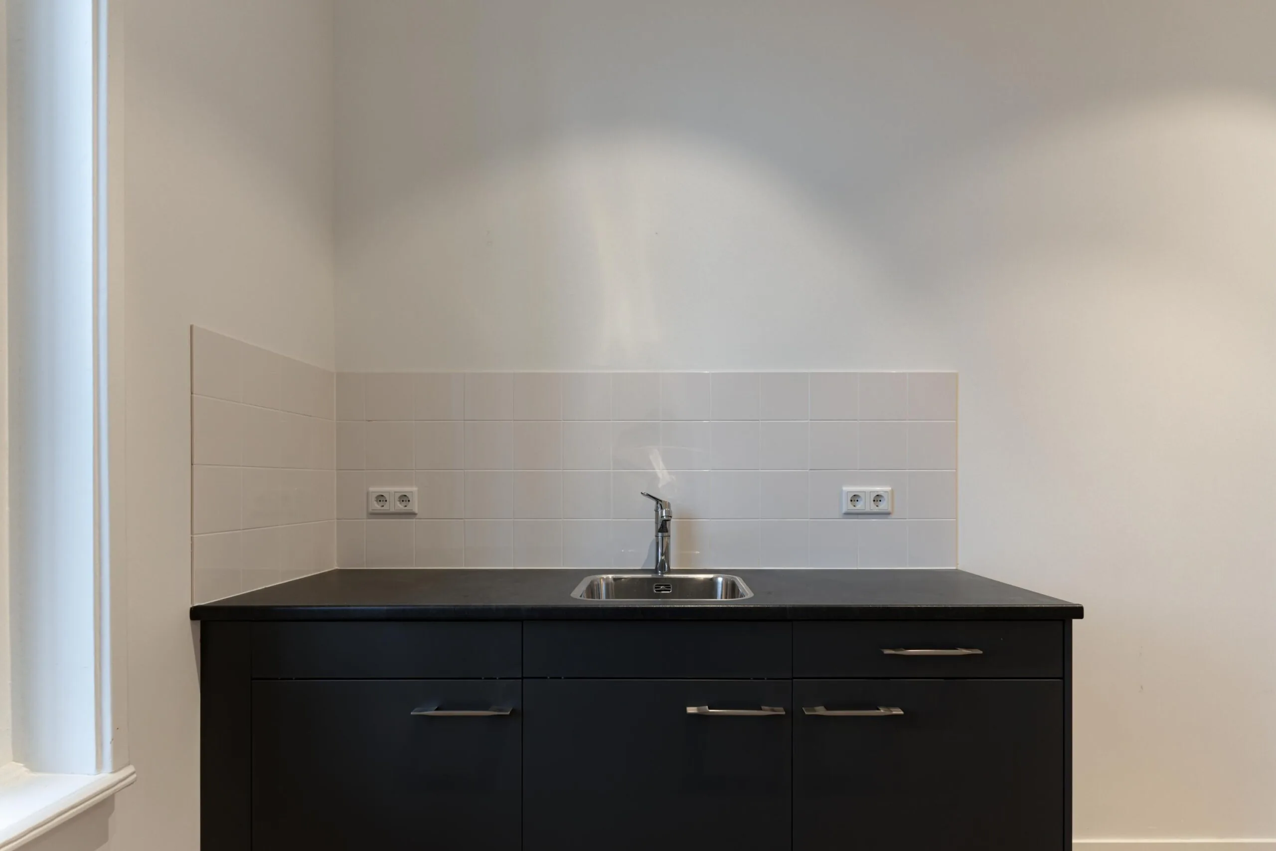 Keukenblok met zwarte kastjes, een rvs spoelbak en witte betegelde achterwand in een woning aan de Biltstraat.