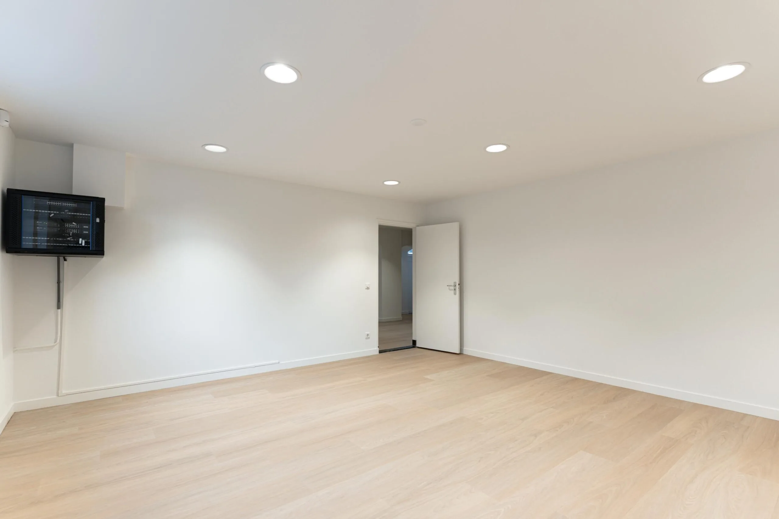 Lege kamer met houten vloer, witte muren, plafondspots en een open deur aan de Biltstraat.