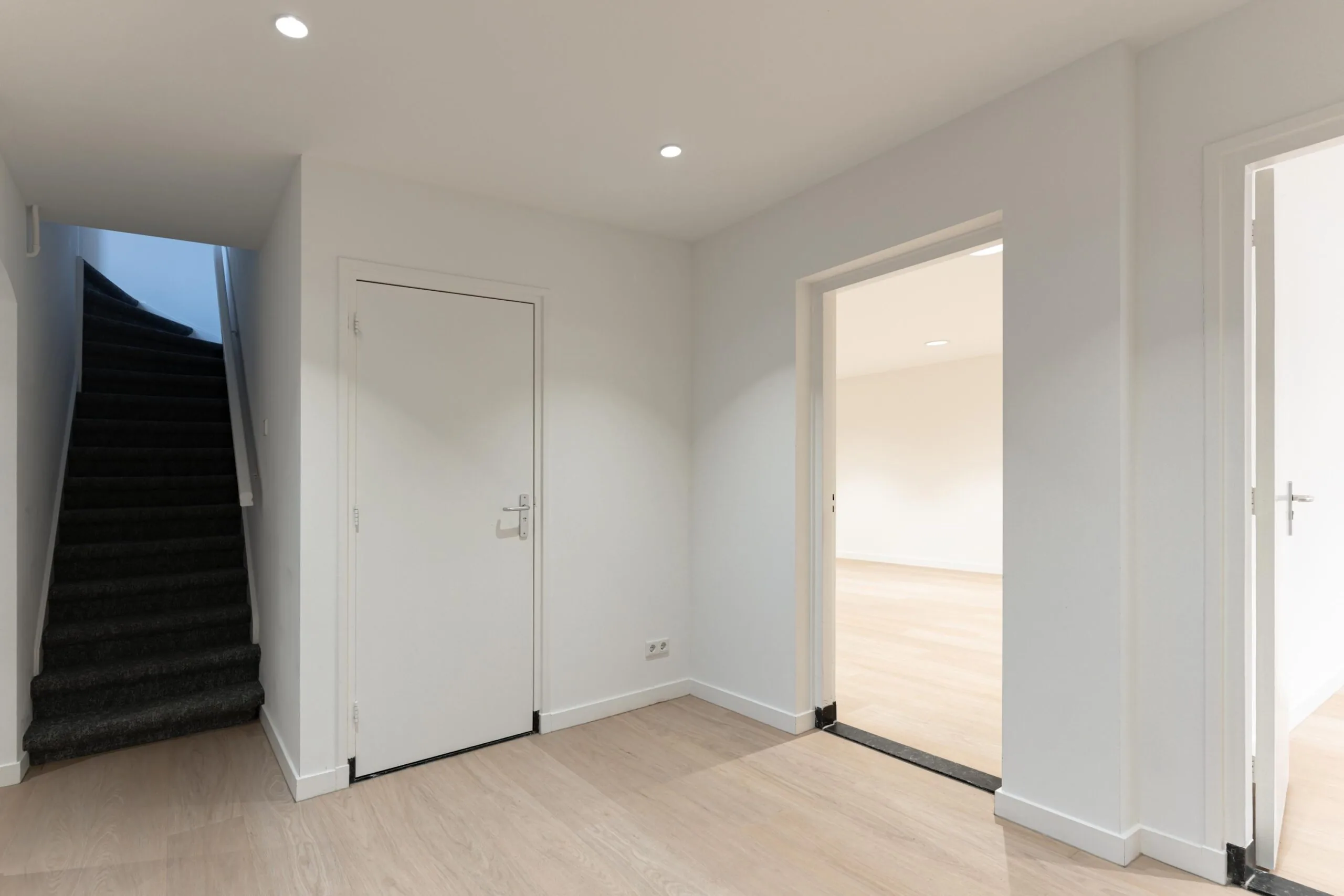 Moderne, lichte hal in een woning aan de Biltstraat met een trap, gesloten deur en twee open doorgangen naar andere kamers.