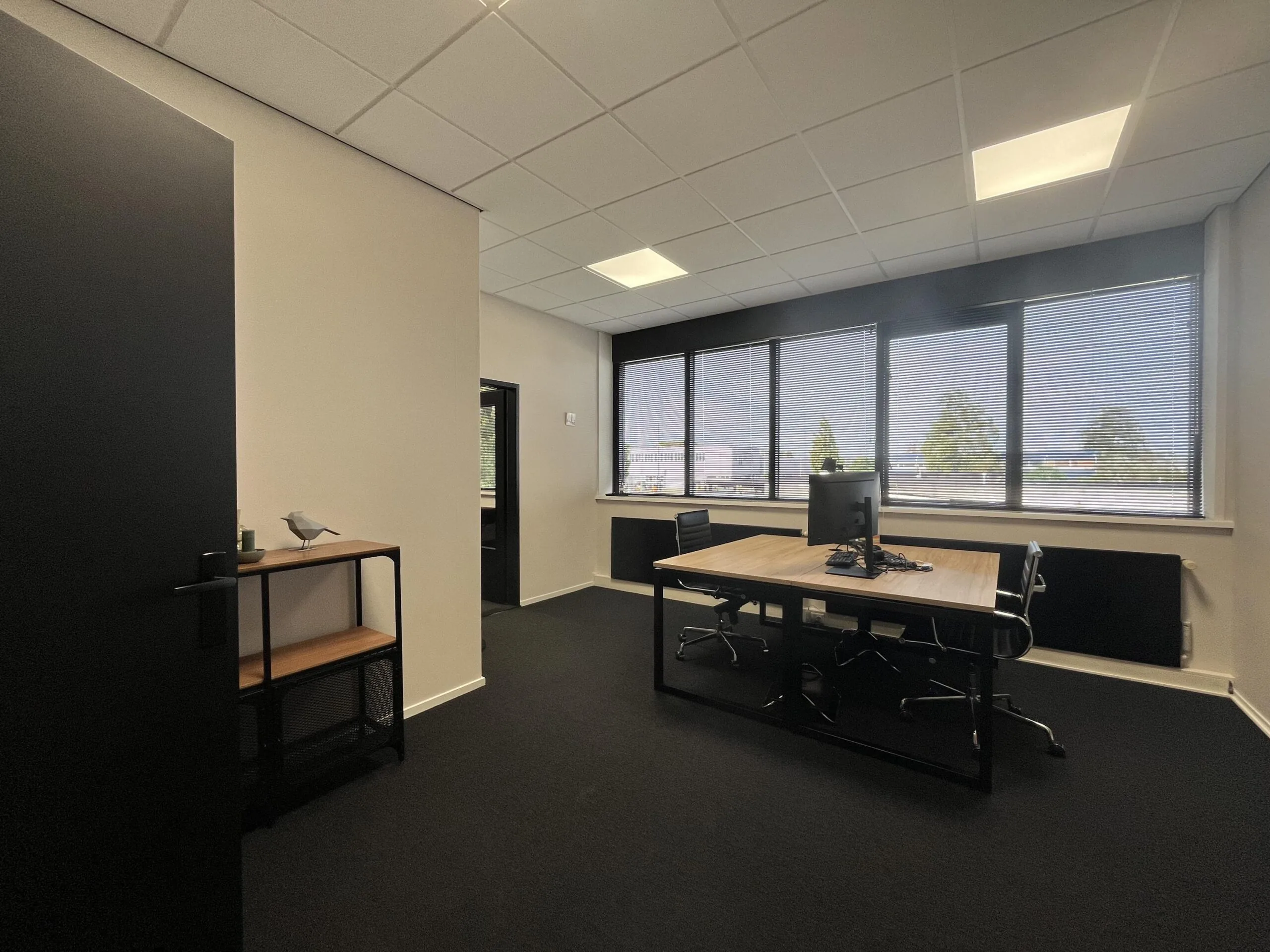 Modern kantoorruimte aan de Industrieweg met bureau, bureaustoelen en groot raam met zonwering.