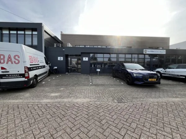 Bedrijfsgebouw aan de Industrieweg 18 met geparkeerde bedrijfswagens en auto's op de oprit.