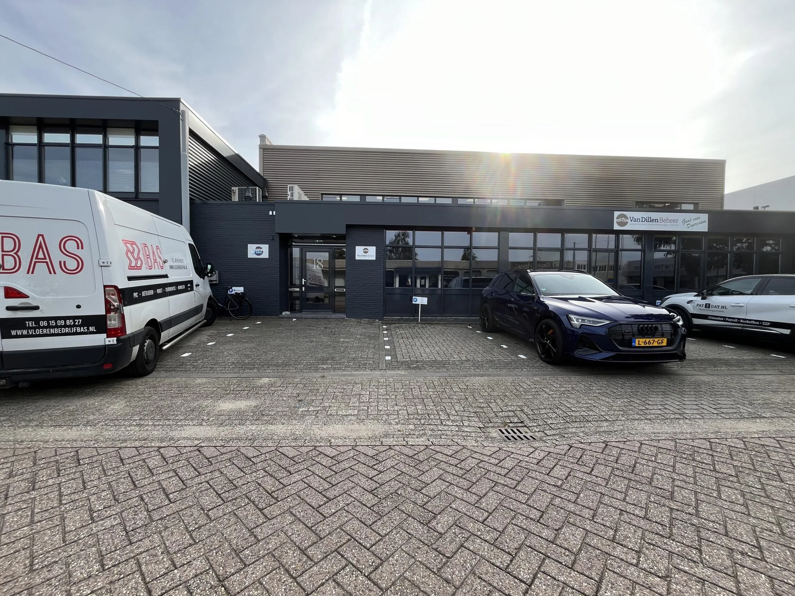 Bedrijfsgebouw aan de Industrieweg 18 met geparkeerde bedrijfswagens en auto's op de oprit.