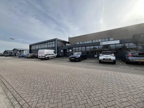 Bedrijfsgebouw aan de Industrieweg met geparkeerde auto's en een bestelbus van BAS voor de ingang van Van Dillen Beheer.