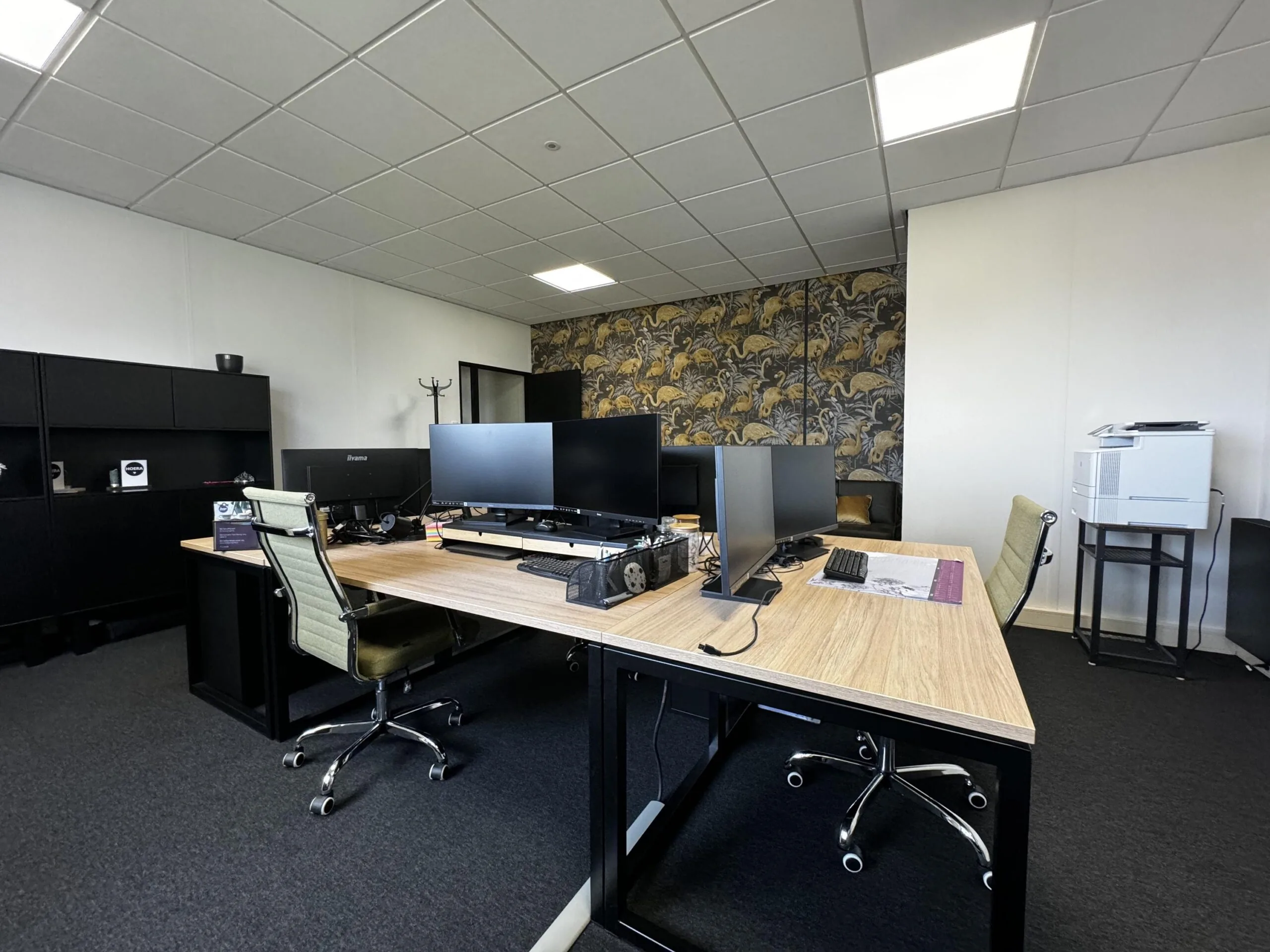 Moderne kantoorruimte aan de Industrieweg met werkplekken, bureaustoelen, computers en een opvallende decoratieve achterwand.