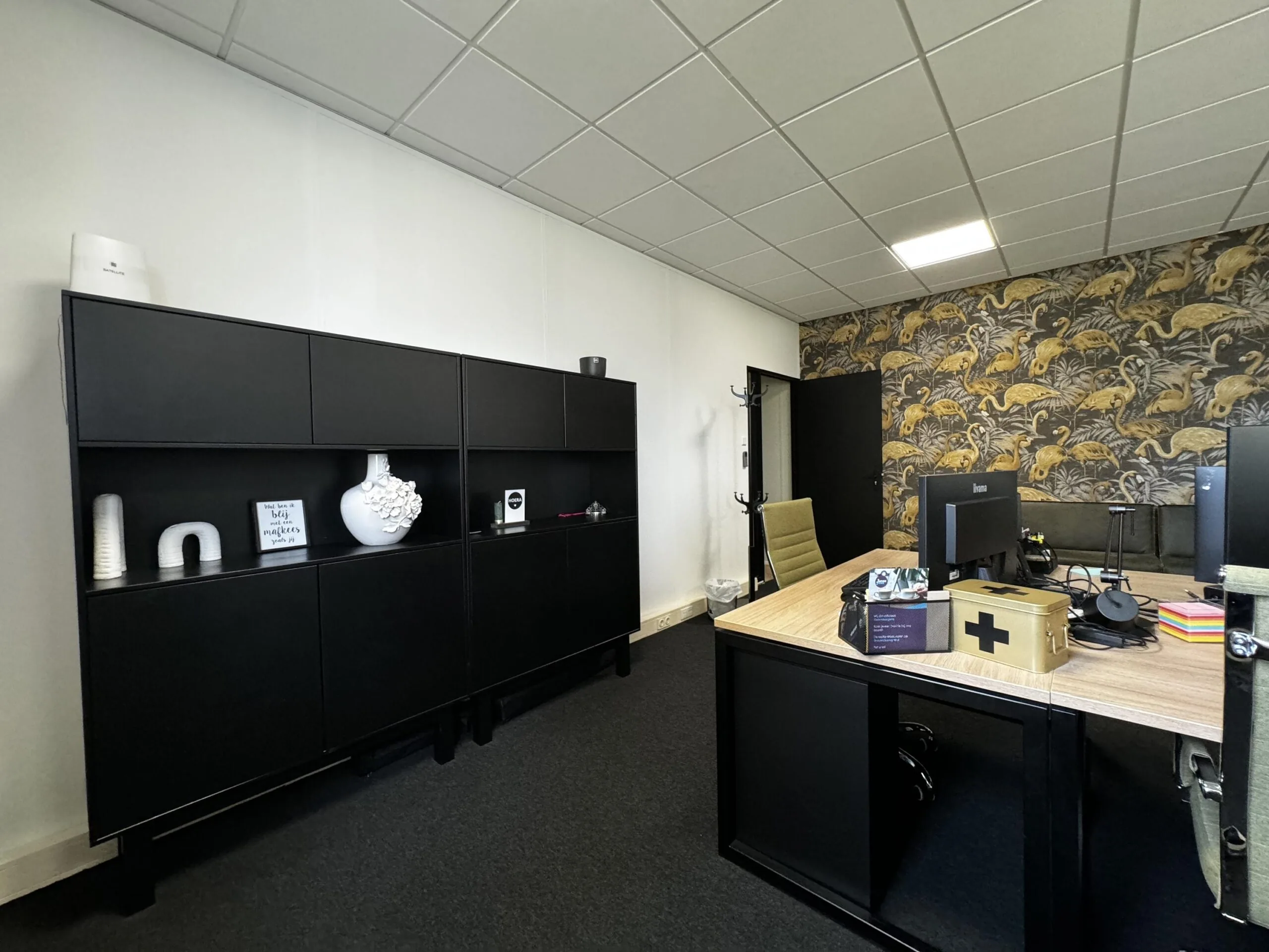 Modern kantoor met een zwart bureau, open kast en een opvallende muur met flamingo-behang.