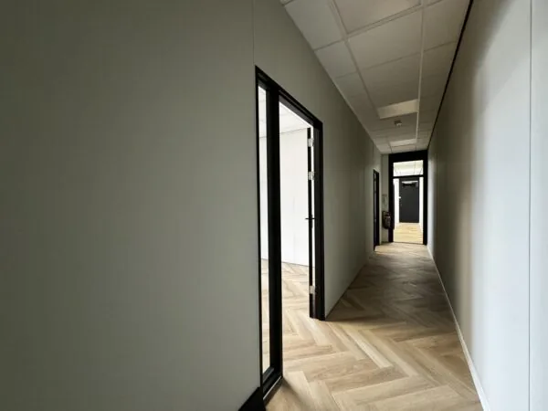 Lichte kantoorhal met visgraatvloer, systeemplafond en zwarte deurkozijnen aan de Industrieweg.