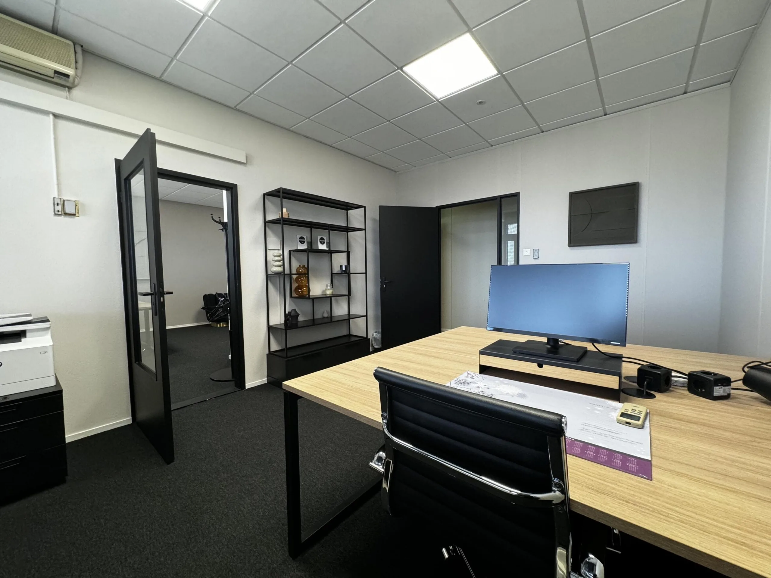 Modern, strak ingericht kantoorbureau aan de Industrieweg met een monitor, bureaustoel en open deur naar een tweede ruimte.