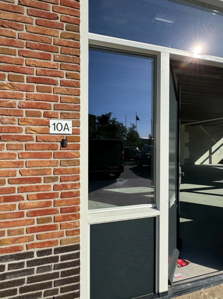 Voordeur van een bedrijfspand aan de Nijverheidslaan 10A met deels open deur en bakstenen gevel.