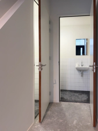 Doorkijk naar een betegelde toiletruimte met een wastafel en spiegel in een gebouw aan de Nijverheidslaan.
