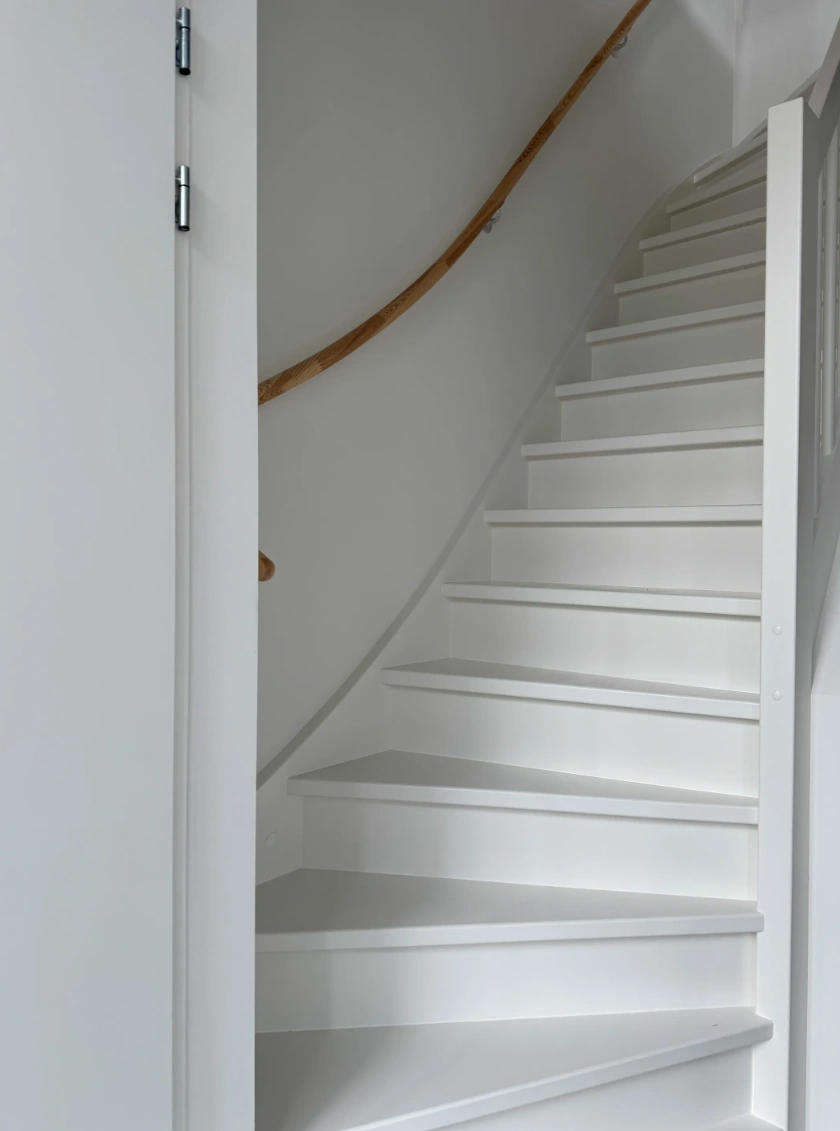 Witte houten trap met een gebogen houten leuning in een modern interieur aan de Nijverheidslaan.