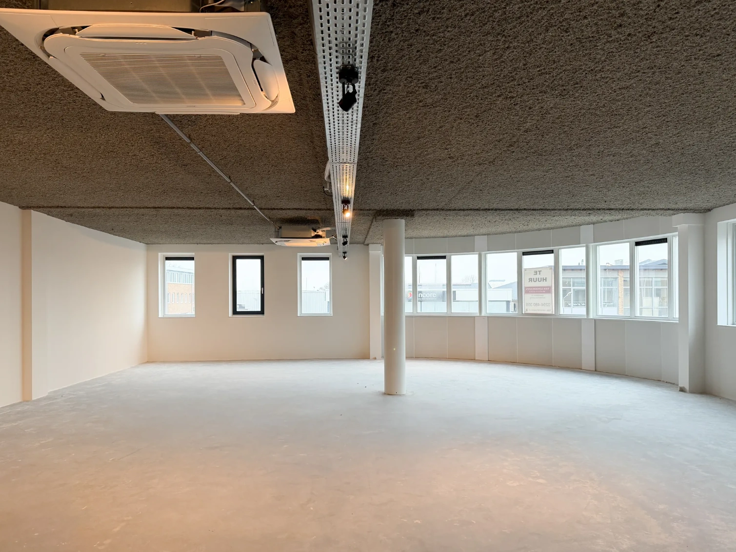 Leeg kantoorpand aan de Nijverheidslaan met grote ramen en betonnen vloer.