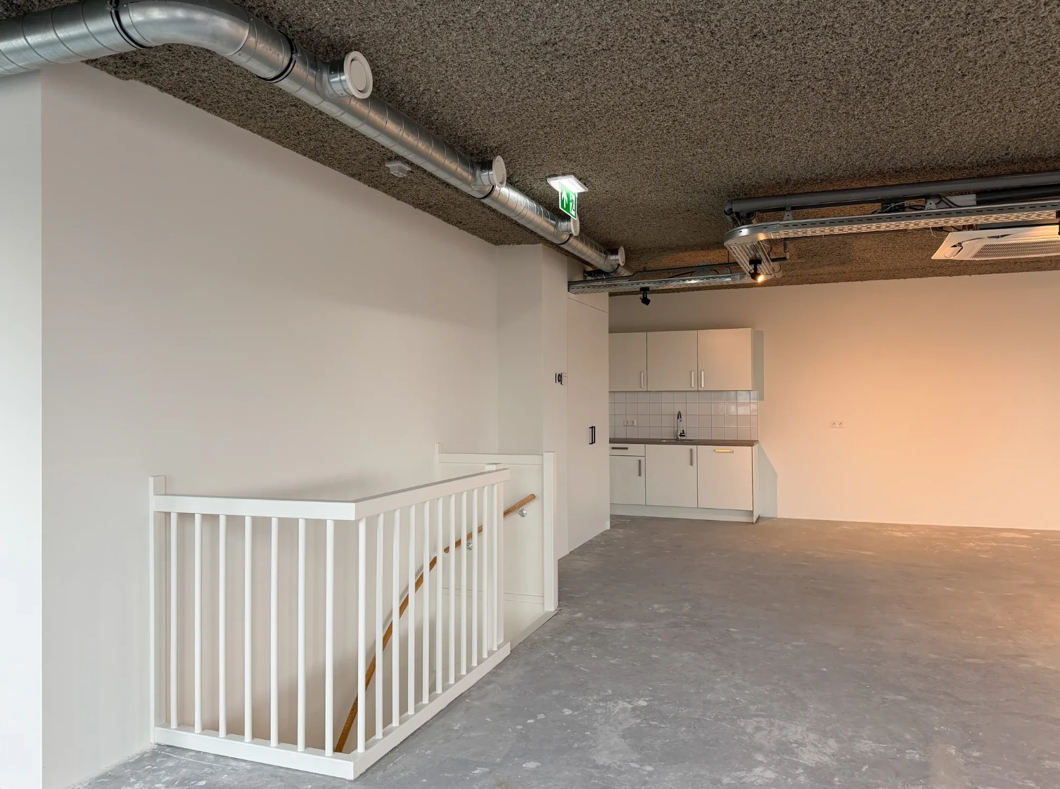 Open bedrijfsruimte aan de Nijverheidslaan met betonnen vloer, zichtbare ventilatiebuizen en een eenvoudige kitchenette.