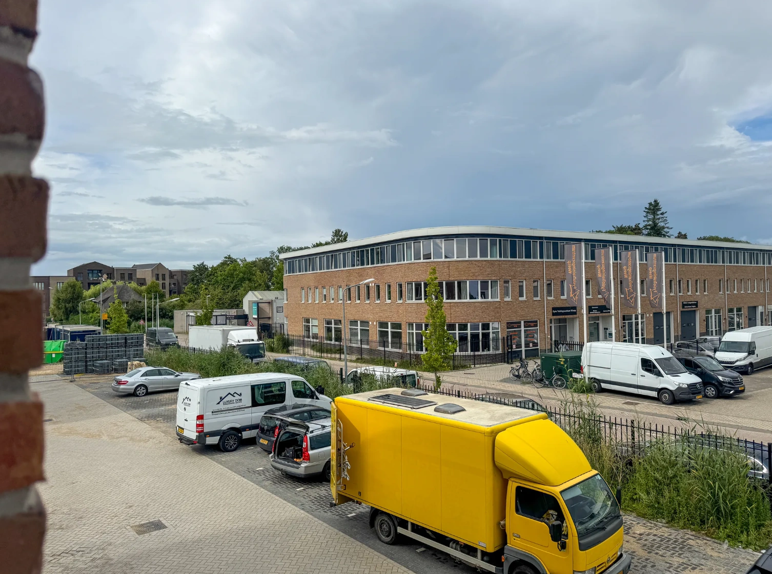 Bedrijfsgebouw aan de Nijverheidslaan met geparkeerde bestelwagens en een opvallende gele vrachtwagen op de voorgrond.