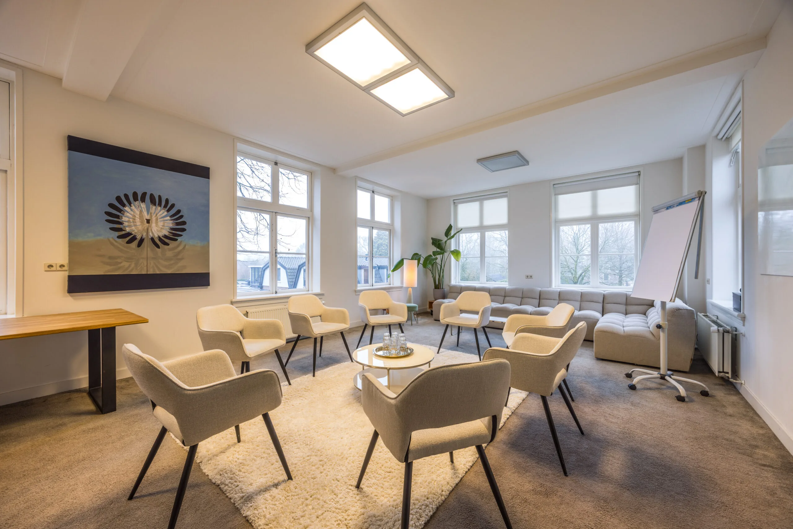 Licht en modern ingerichte vergaderruimte met een kring van stoelen, een flip-over en een groot kunstwerk aan de muur.
