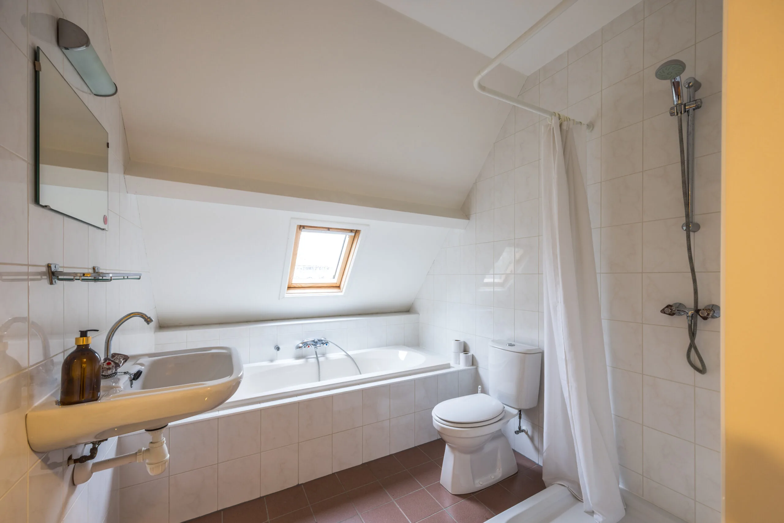 Badkamer met ligbad onder een schuin dakraam, toilet, douche en wastafel.