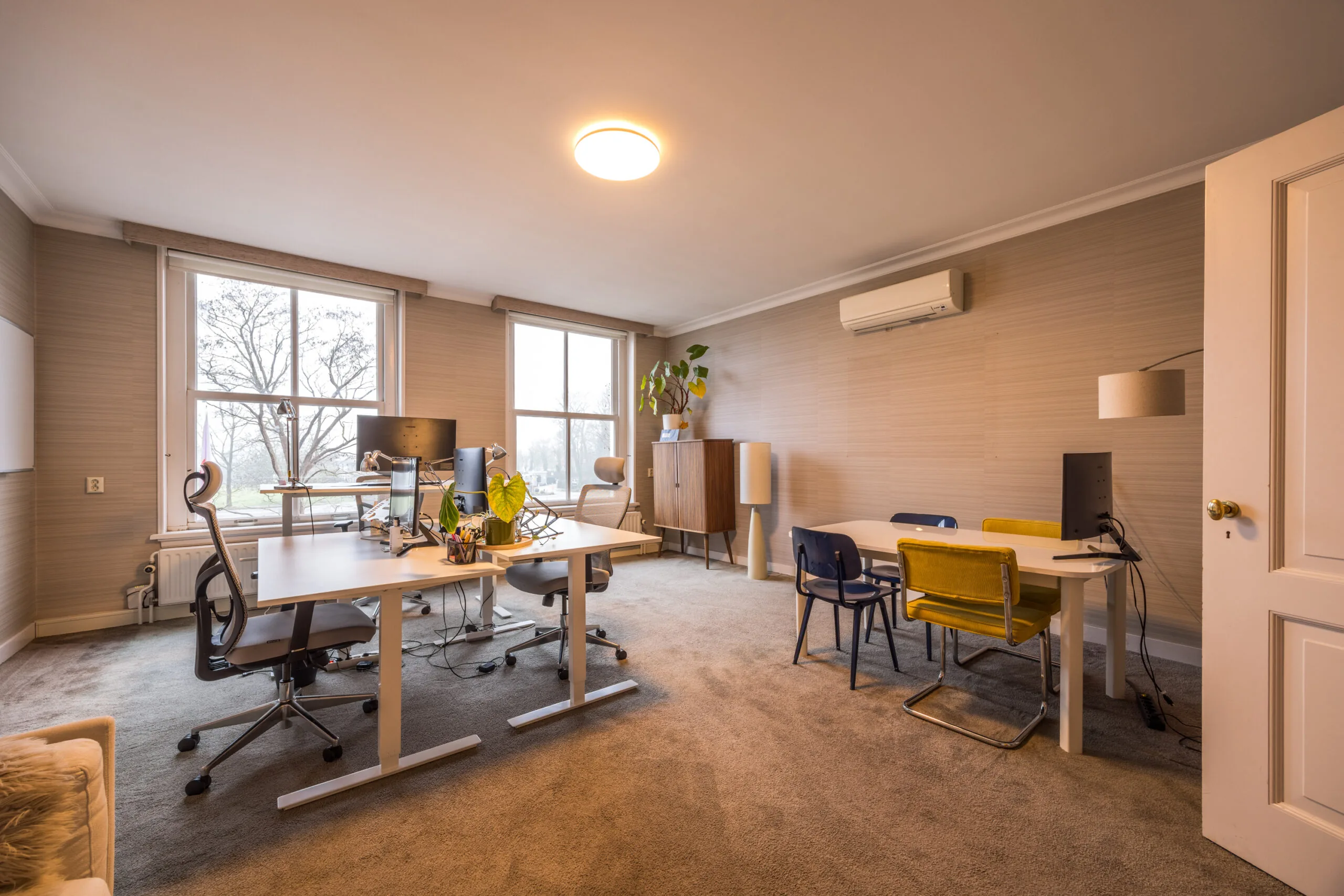 Modern kantoor met bureaus en stoelen, grote ramen en warme verlichting in een ruimte aan het Zandpad.