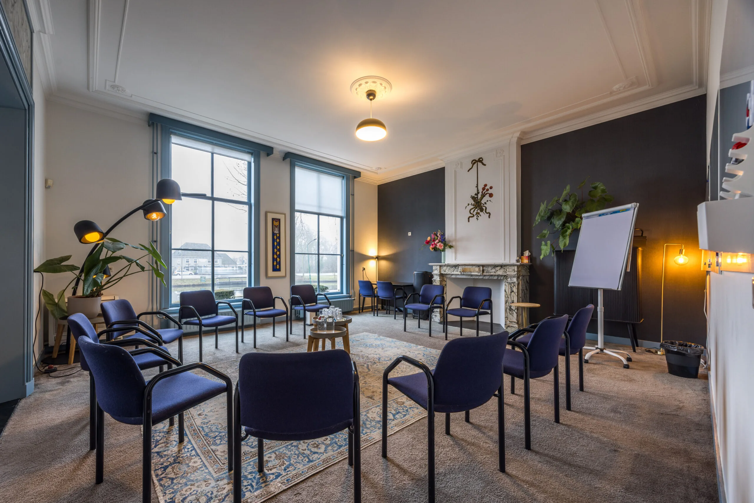 Vergaderruimte met een kring van blauwe stoelen, een flip-over en grote ramen in een sfeervolle setting aan het Zandpad.
