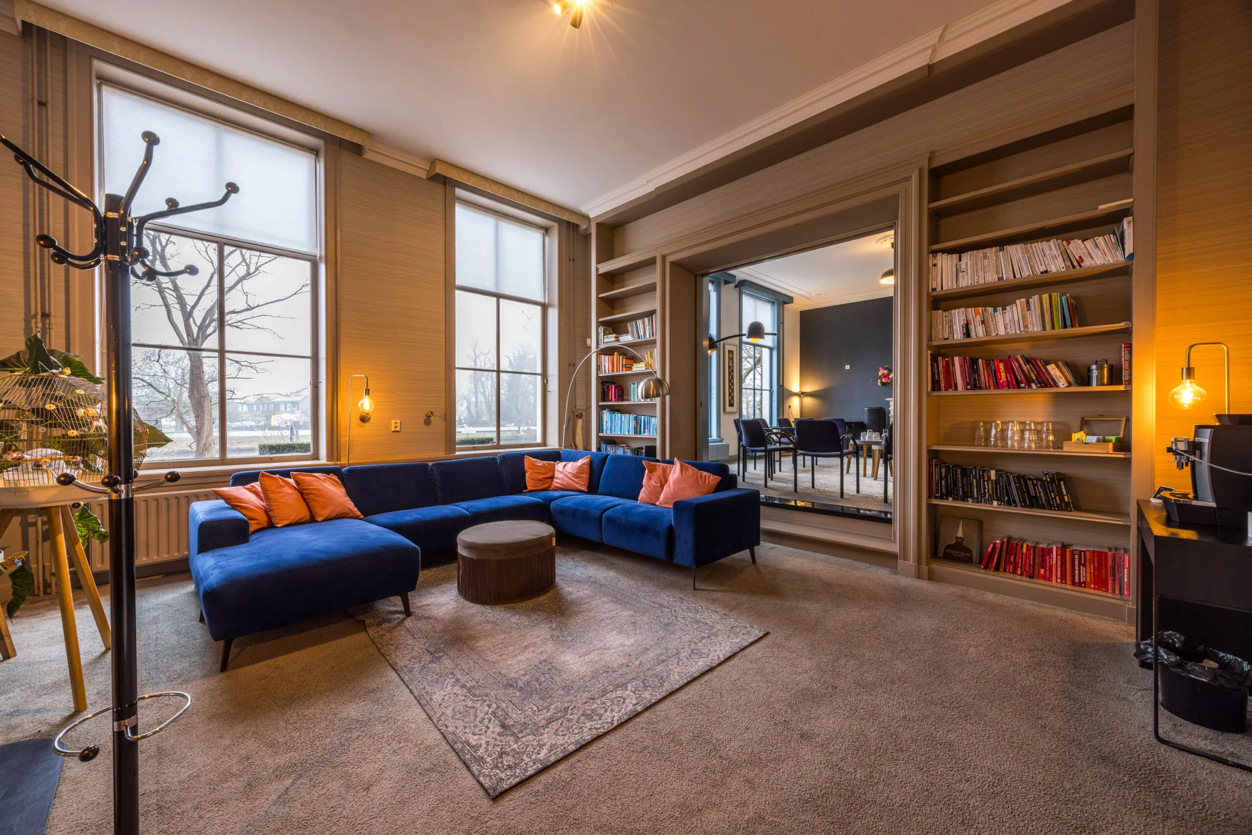 Stijlvol ingerichte lounge met een blauwe hoekbank, boekenplanken en grote ramen aan het Zandpad.