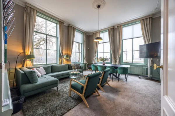 Stijlvol ingerichte woonkamer met groene meubels, grote ramen en een eettafel met zes stoelen.
