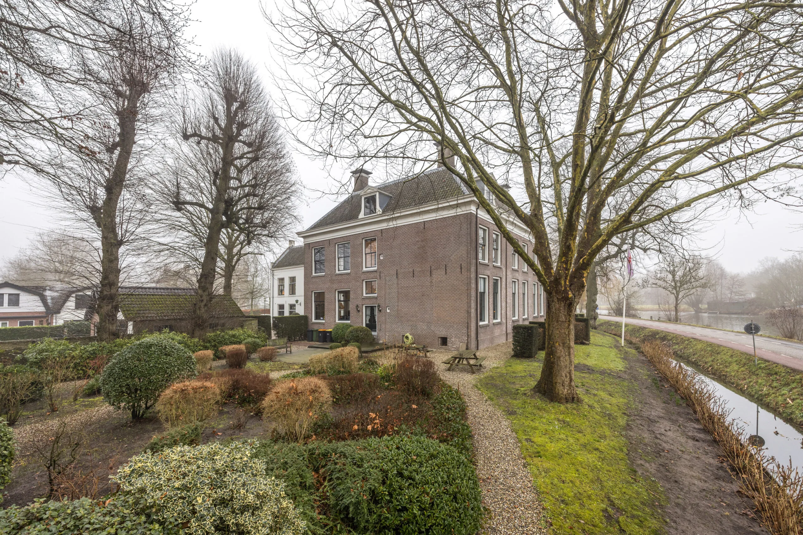 Een klassiek herenhuis aan het Zandpad met verzorgde tuin en zicht op een kanaal op een mistige dag.