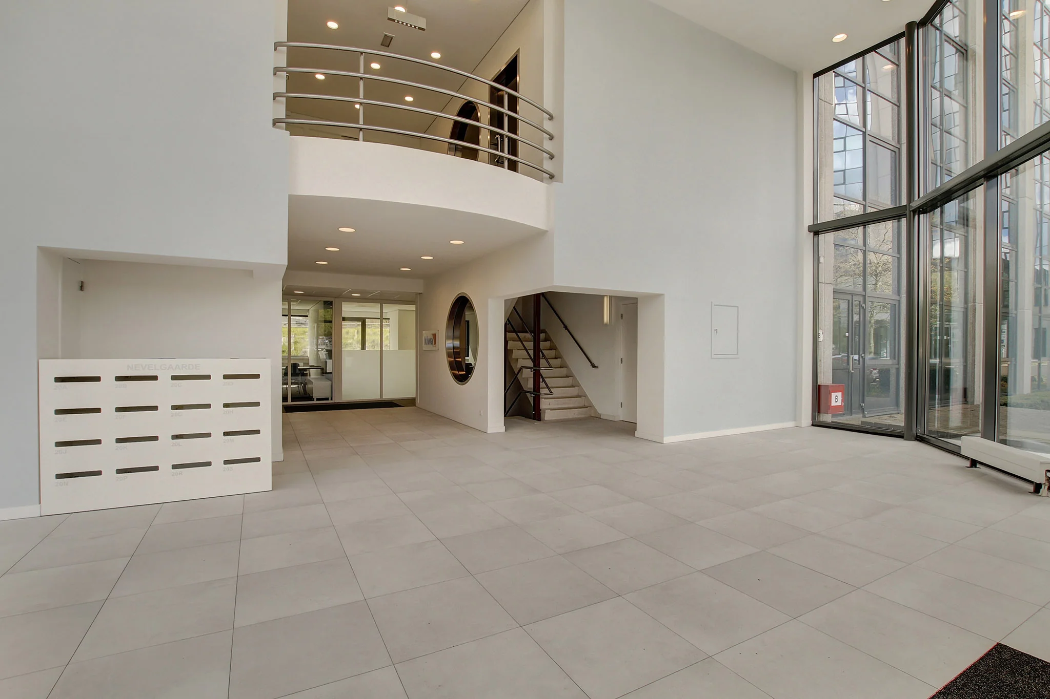Moderne, lichte entreehal van een kantoorgebouw aan de Nevelgaarde met trappenhuis, brievenbussen en glazen gevel.
