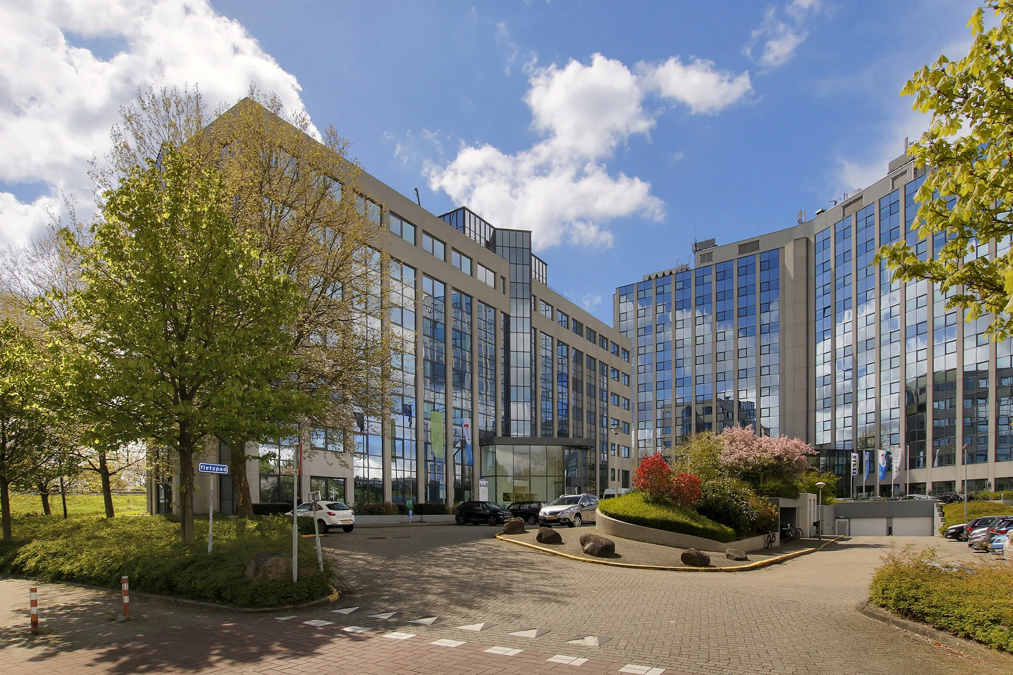 Modern kantoorpand aan de Nevelgaarde in Nieuwegein met glazen gevels en omliggende bomen en parkeerplaatsen.