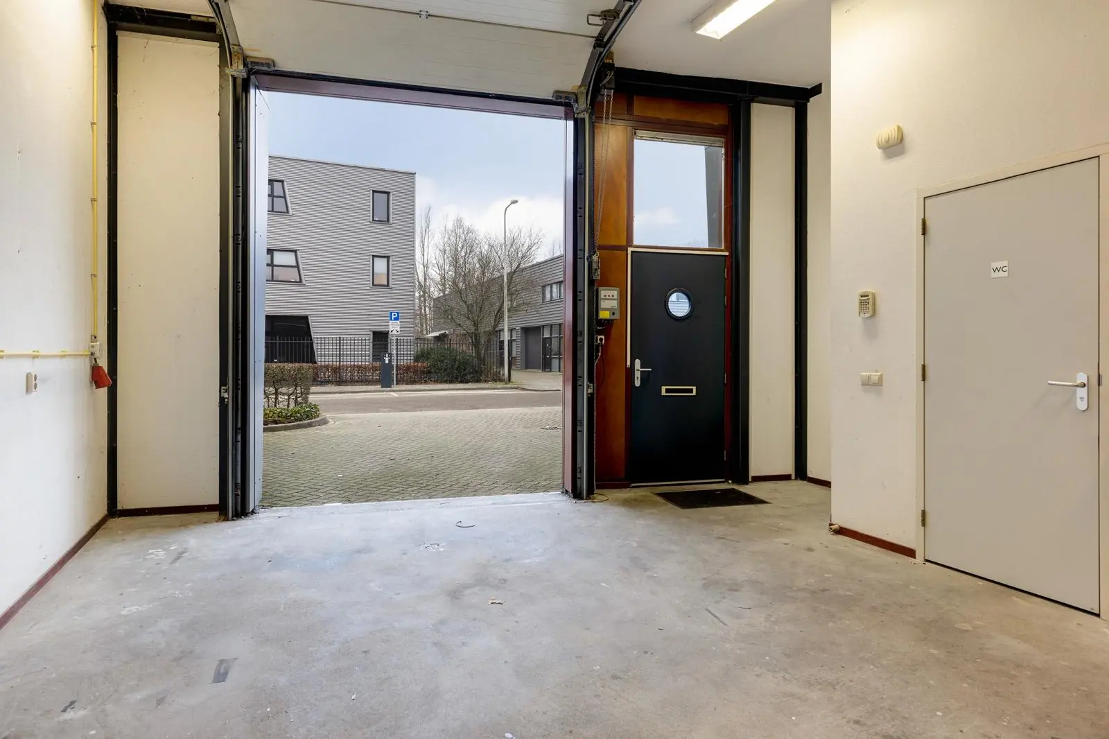 Interieur van een lege garage aan de Tennesseedreef met open garagedeur, voordeur en deur naar het toilet.
