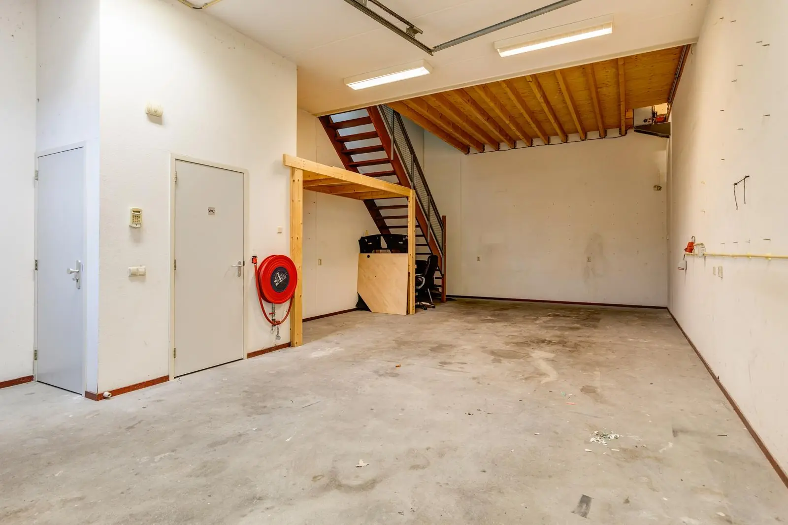 Leegstaand bedrijfspand aan de Tennesseedreef met betonnen vloer, trap naar entresol en brandslanghaspel aan de muur.