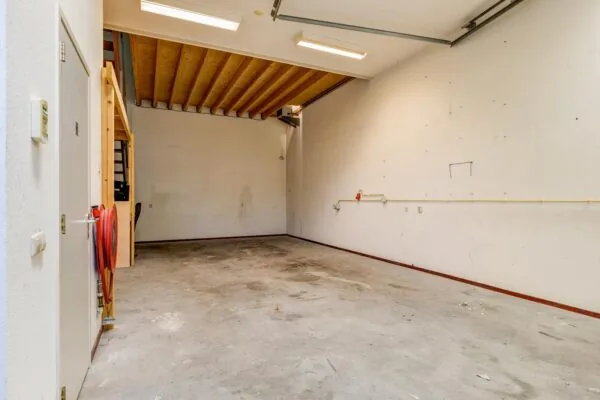 Lege garage of opslagruimte aan de Tennesseedreef met betonnen vloer, houten zoldering en trap naar een entresol.