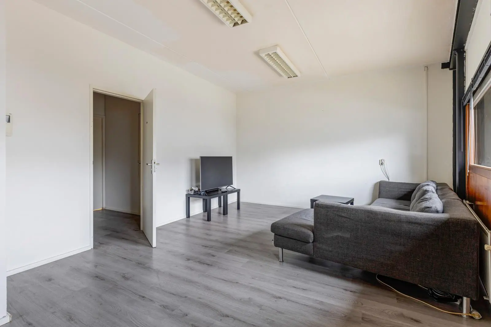 Woonkamer in een woning aan de Tennesseedreef met een grijze hoekbank, televisie en laminaatvloer.
