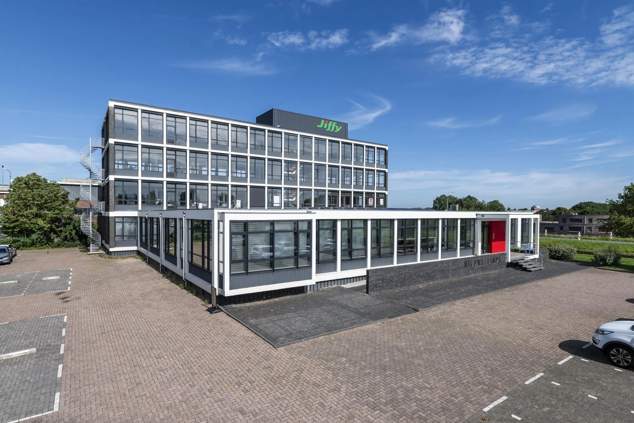 Modern kantoorgebouw aan de Lindtsedijk met het logo van Jiffy op het dak en een parkeerterrein op de voorgrond.