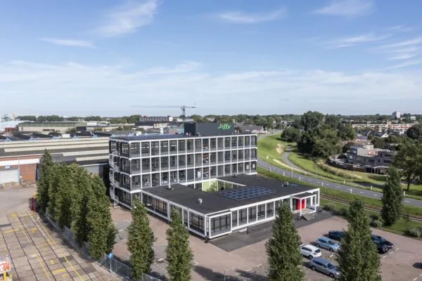 Luchtfoto van een modern kantoorgebouw aan de Lindtsedijk met het logo van Jiffy op het dak, omringd door bomen en een industriële omgeving.