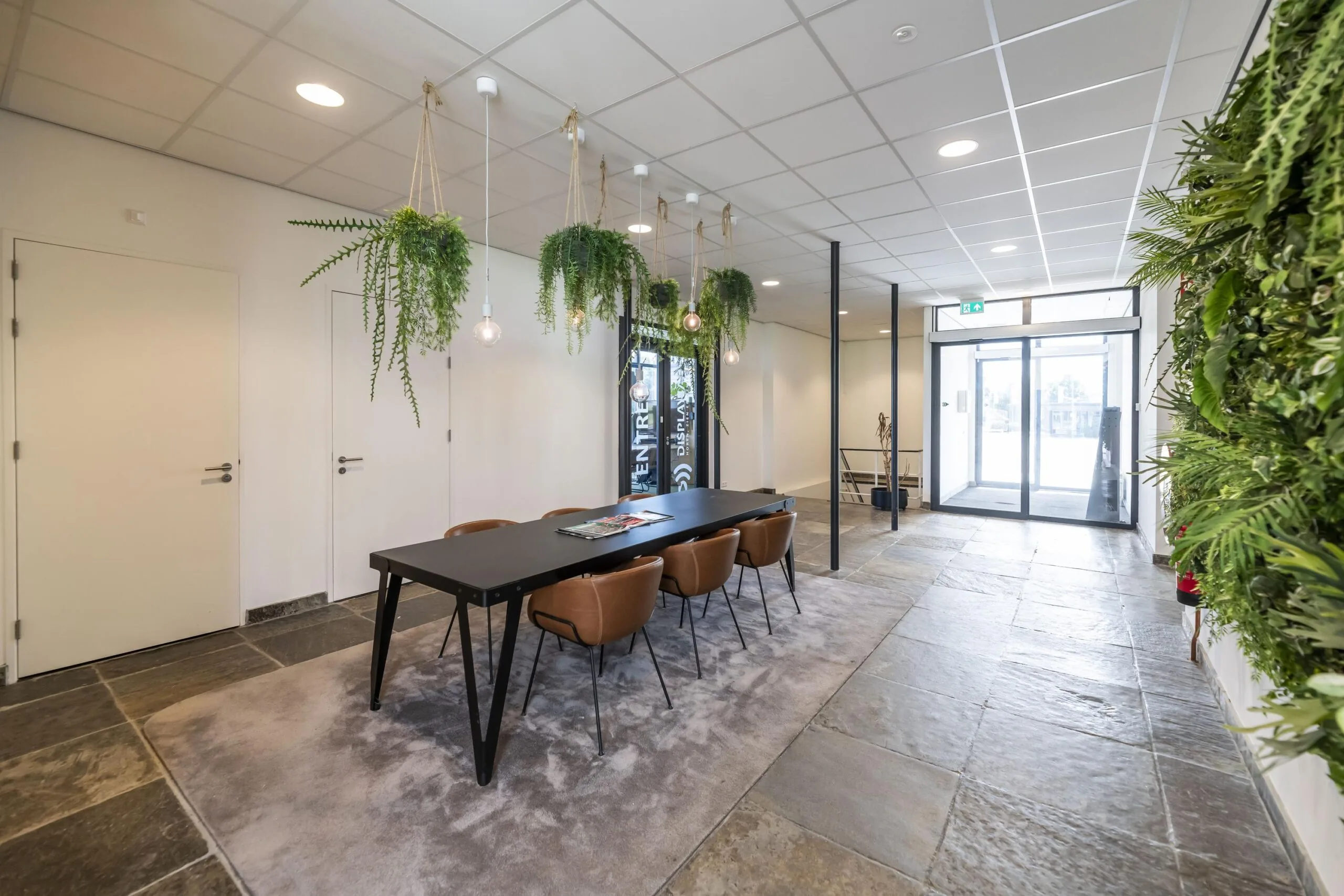 Moderne entreehal aan de Lindtsedijk met een vergadertafel, hangplanten en een groene wand.