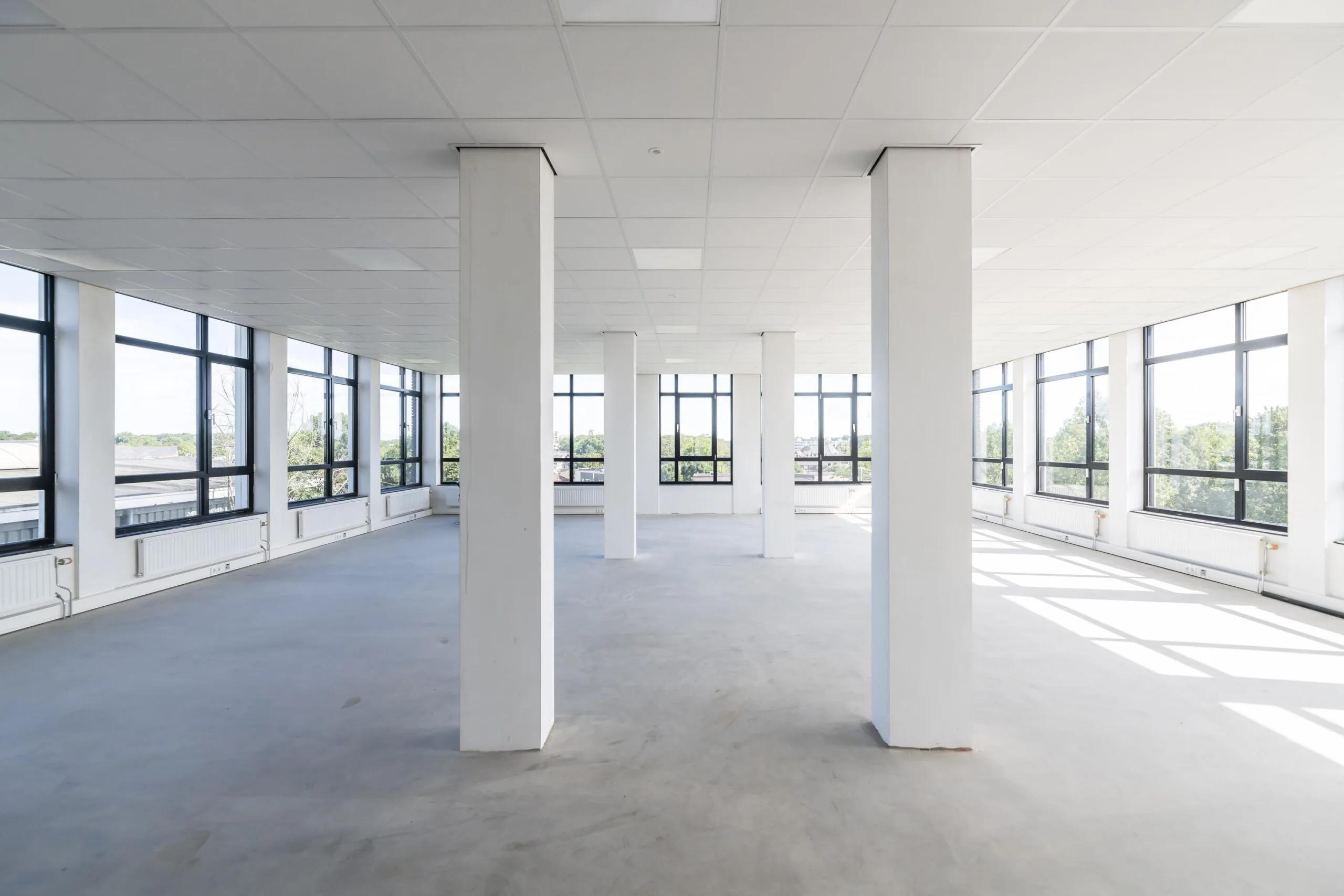 Licht en open leegstaand kantoorpand aan de Lindtsedijk met grote ramen en betonnen vloer.