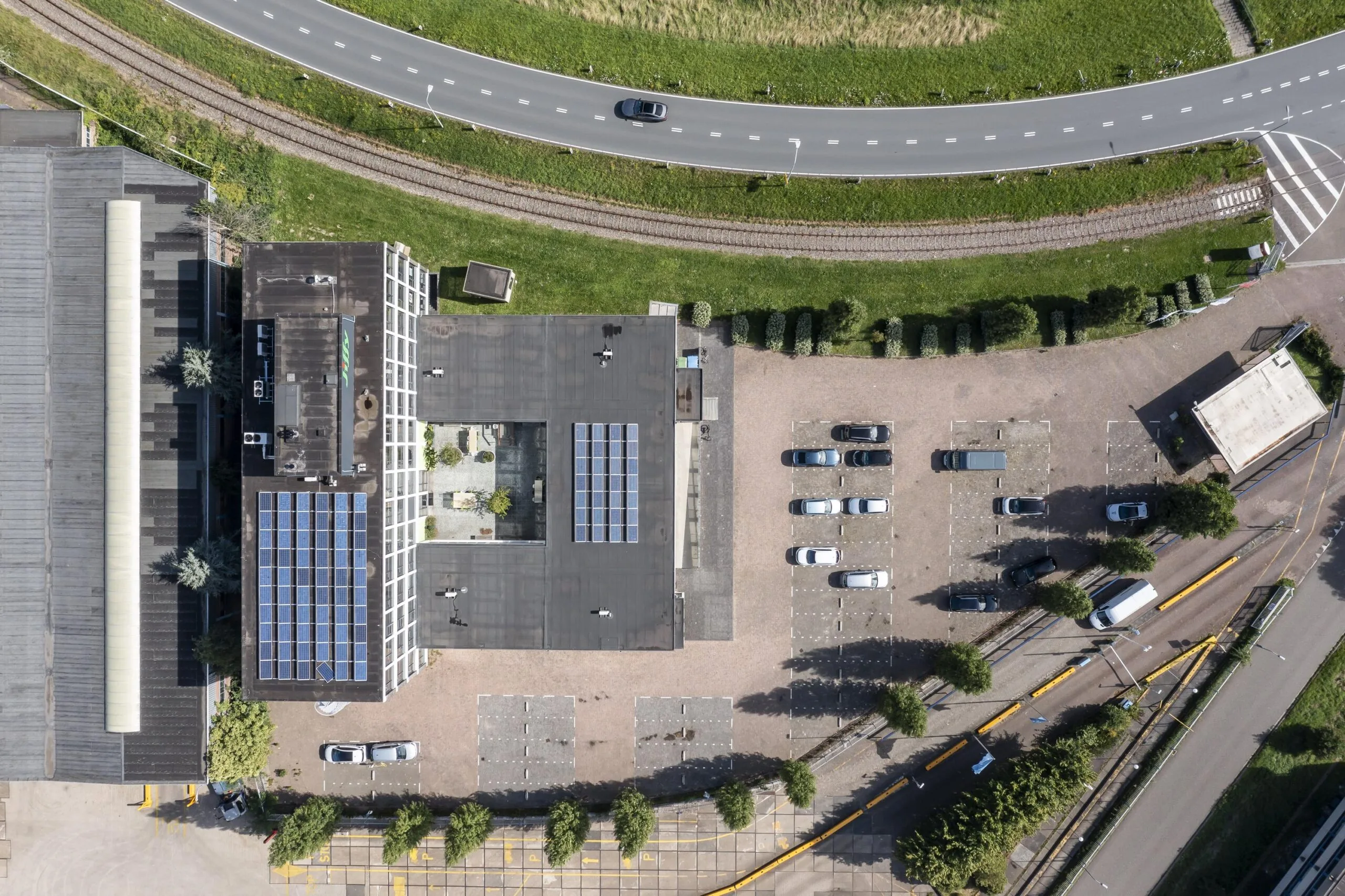 Luchtfoto van een gebouw aan de Lindtsedijk met zonnepanelen op het dak en een naastgelegen parkeerterrein.