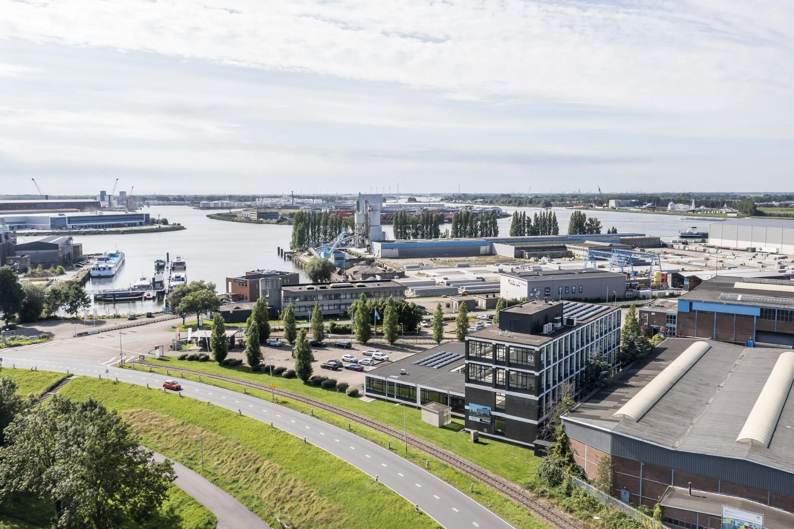 Luchtfoto van het bedrijventerrein aan de Lindtsedijk in Zwijndrecht met uitzicht op de rivier en omliggende bedrijfshallen.