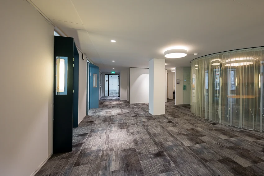 Een moderne, lichte kantoorgang met blauwe accenten en een ronde glazen ruimte.