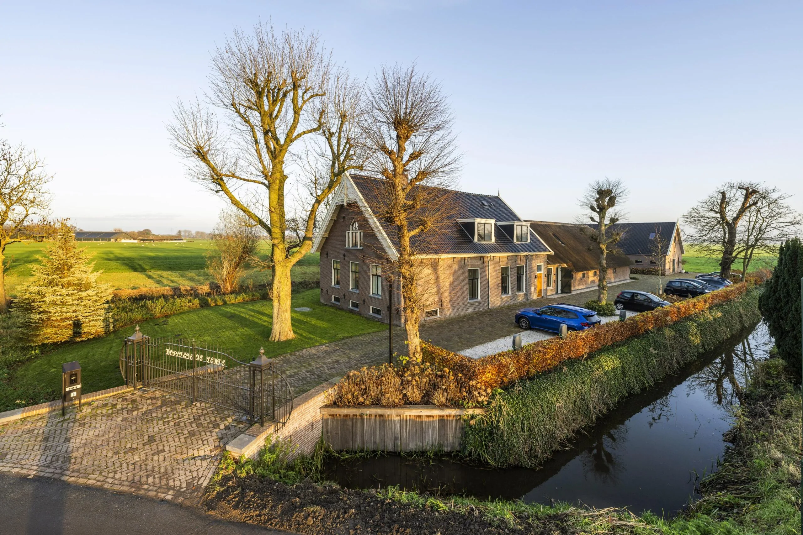 Boerderij De Vrede aan Gein-Zuid met oprit, geparkeerde auto's en omringend polderlandschap in het zonlicht.