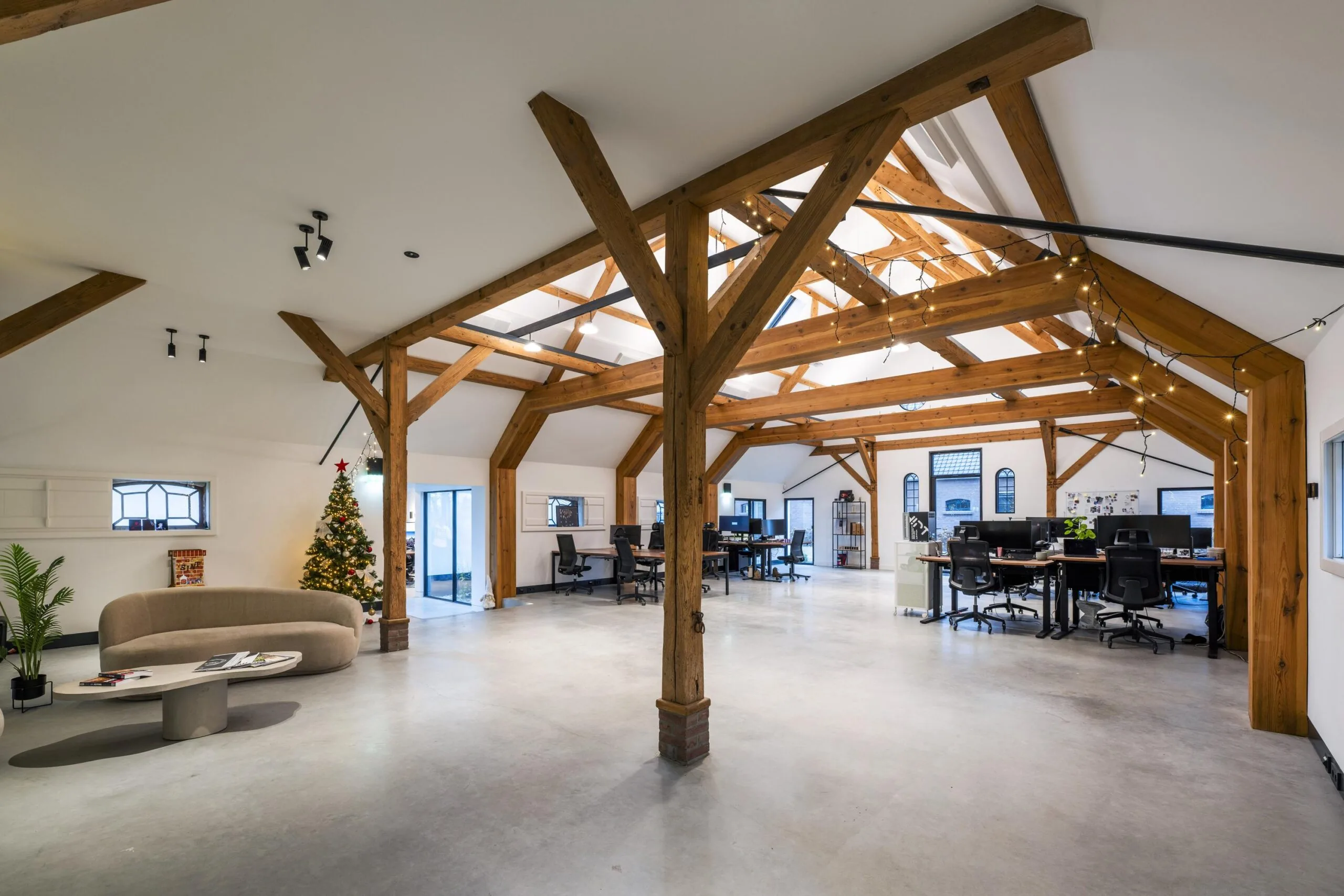Modern kantoor in boerderijstijl met houten balken, open werkplekken en een kerstboom.