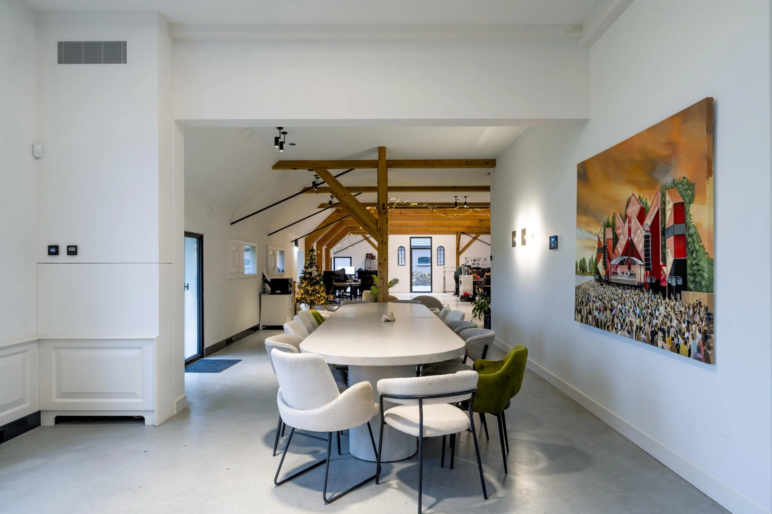 Moderne vergaderruimte met een lange tafel, designstoelen, houten balken en een schilderij van festival Gein-Zuid aan de muur.