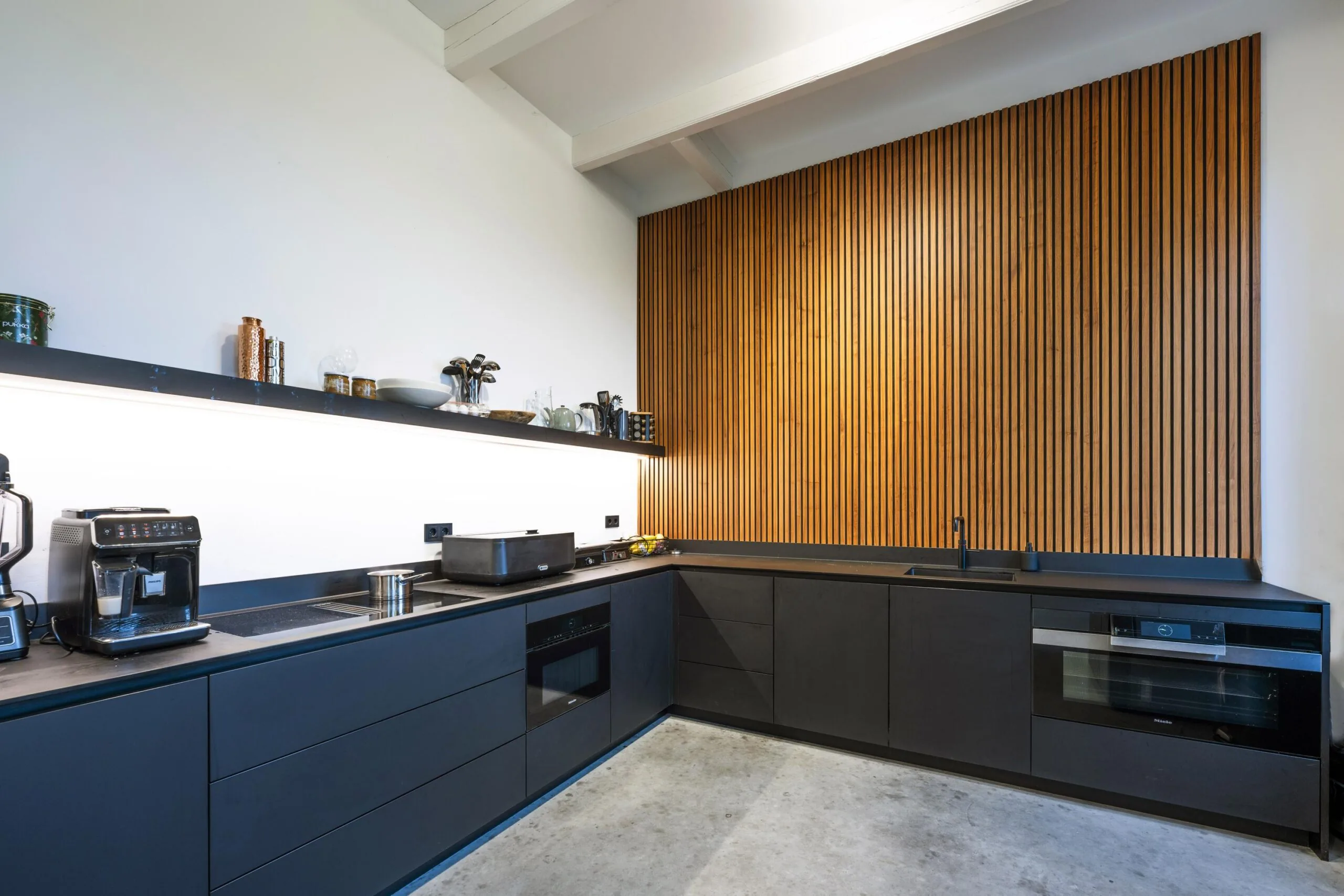 Moderne zwarte keuken in Gein-Zuid met houten lattenwand en strakke inbouwapparatuur.