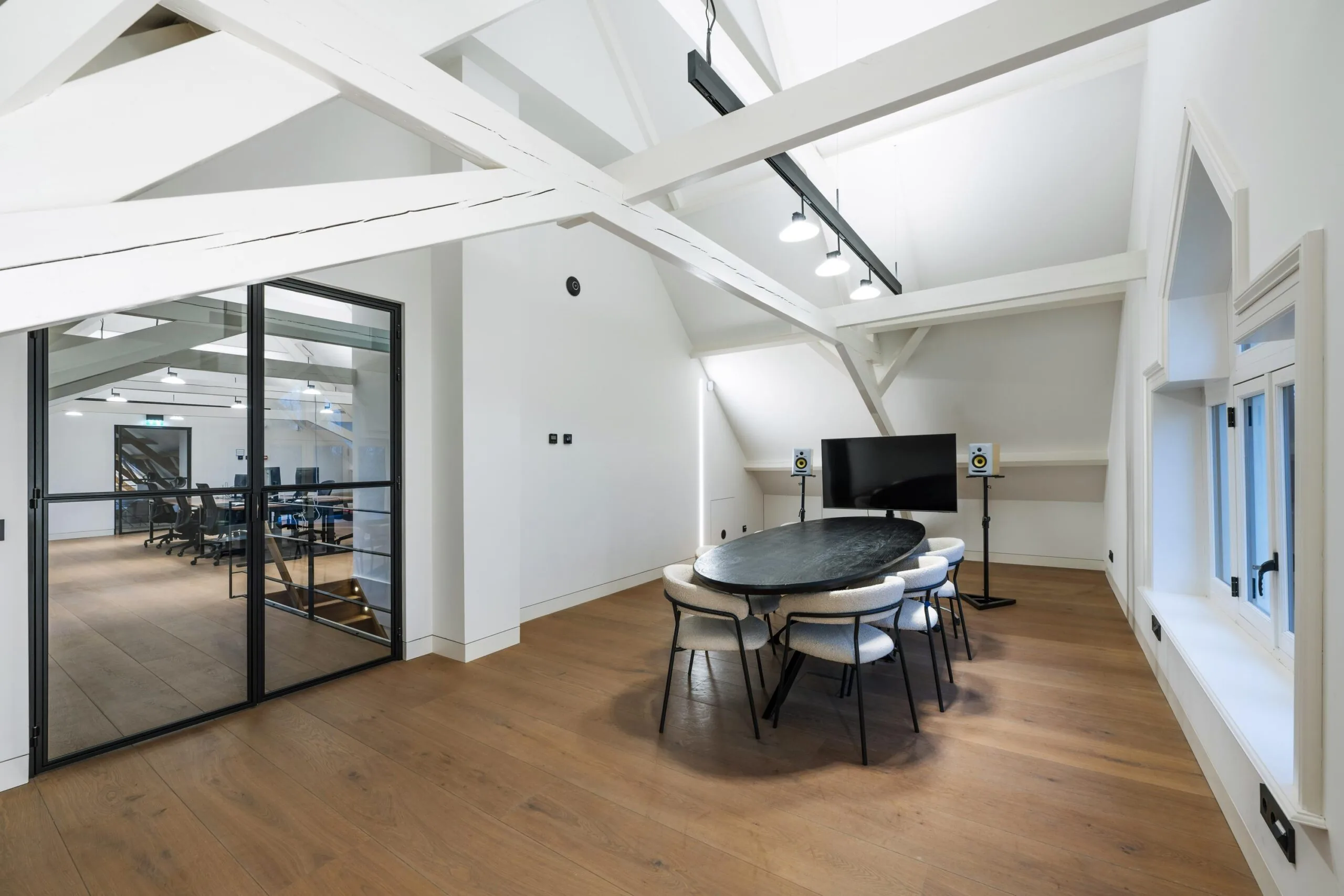 Moderne vergaderruimte in Gein-Zuid met houten vloer, ovale tafel, presentatiescherm en zicht op een open kantoorruimte.