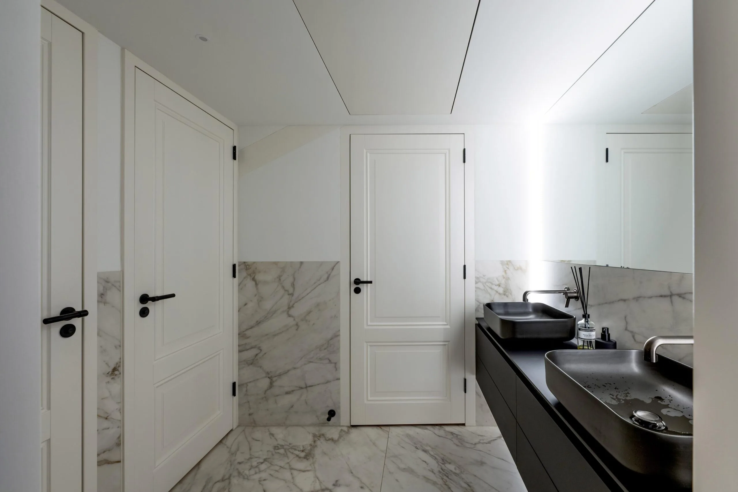 Moderne badkamer in Gein-Zuid met zwart wastafelmeubel, marmeren vloer en muren, en strakke witte deuren.