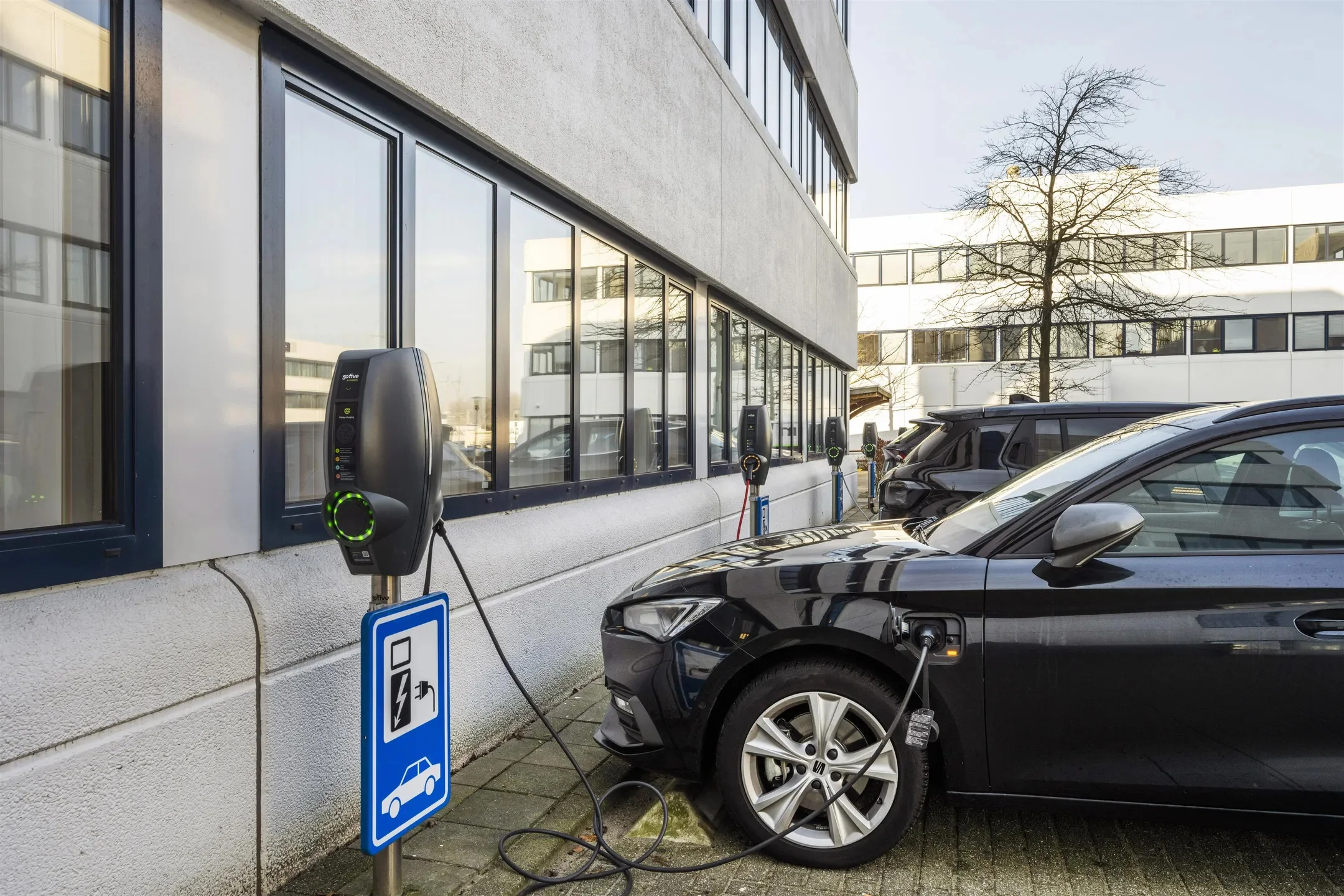 Elektrische auto’s staan geparkeerd en worden opgeladen bij laadpalen naast een kantoorgebouw aan de Kobaltweg.