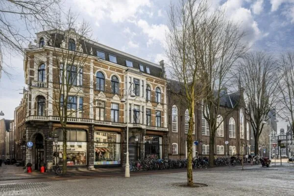 Een hoekpand aan de Handboogstraat met een historische gevel, omringd door bomen en geparkeerde fietsen.