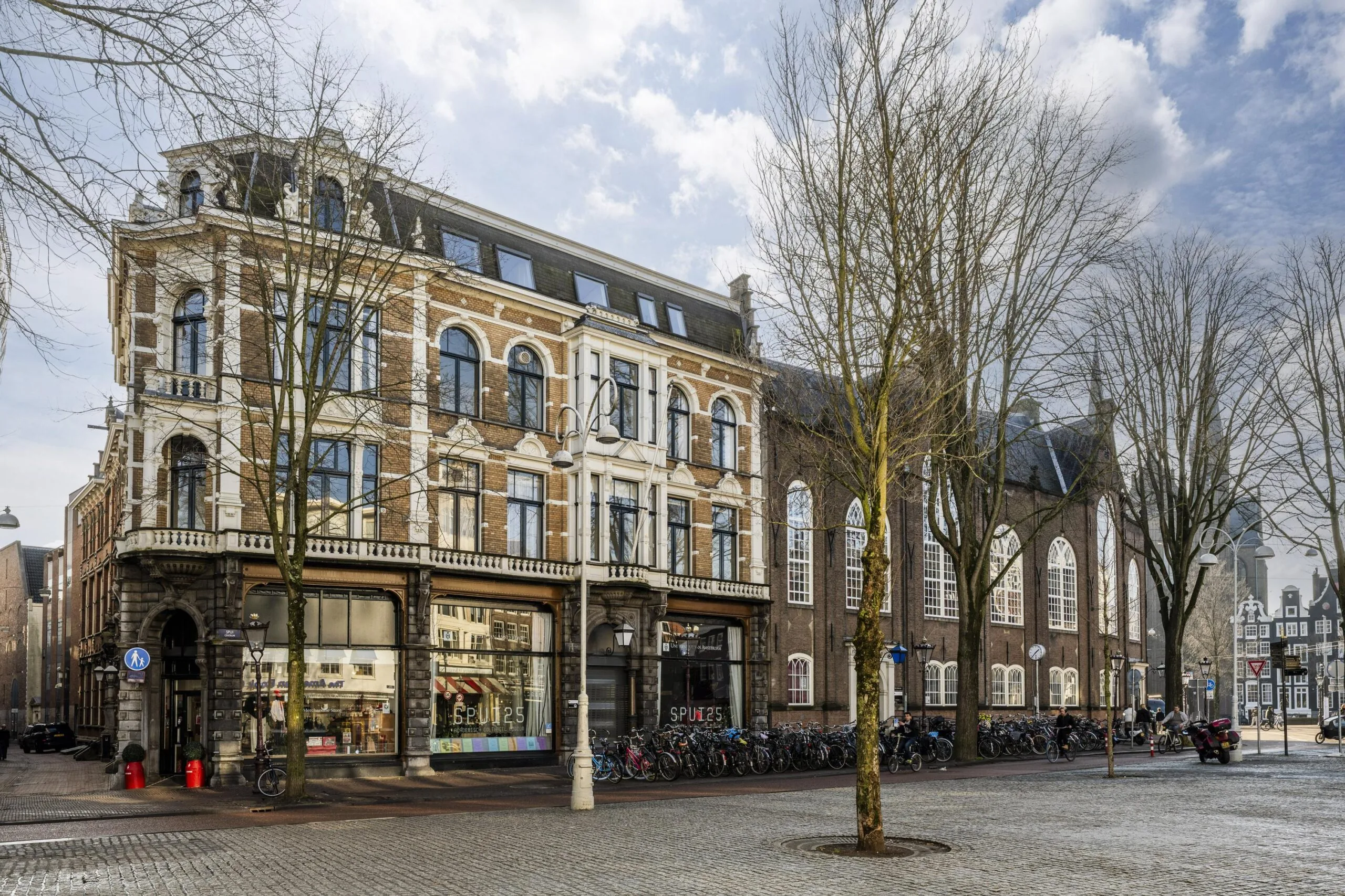 Een hoekpand aan de Handboogstraat met een historische gevel, omringd door bomen en geparkeerde fietsen.