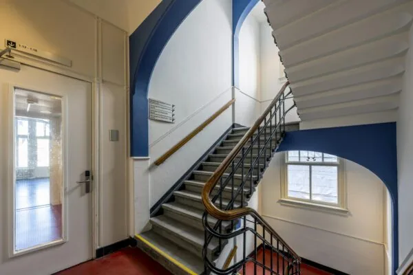 Trap in een gebouw met blauwe accenten en een bord met route-indicaties aan de muur.