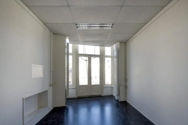 Leeg kantoor met witte muren en grote ramen die uitkijken op de straat.