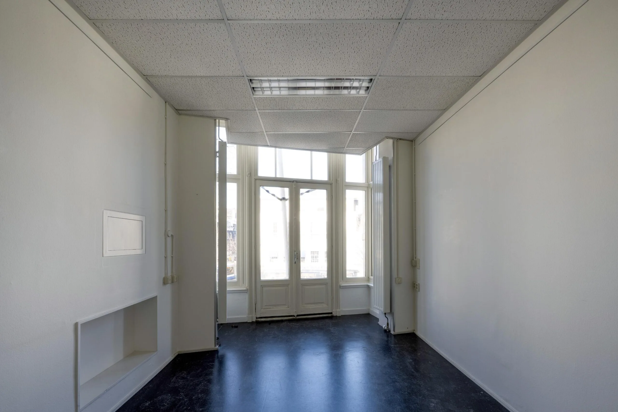 Leeg kantoor met witte muren en grote ramen die uitkijken op de straat.